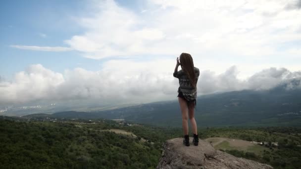 Ένα μοναχικό κορίτσι με αθλητικές μαύρες μπότες στέκεται σε ένα ψηλό λόφο στα βουνά — Αρχείο Βίντεο