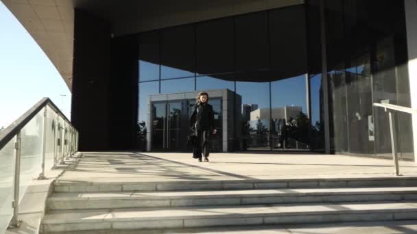 Eine Frau im Hosenanzug geht aus einem Bürogebäude die Treppe hinunter — Stockvideo