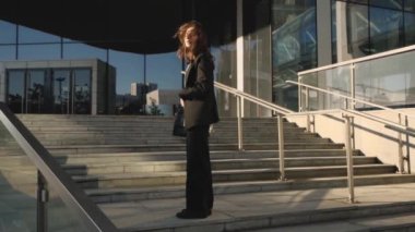 Modern bir iş kadını cam ofis binasının merdivenlerinde duruyor.