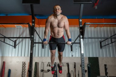 A strong brutal man in sports shorts performs an exercise on a gym simulator.