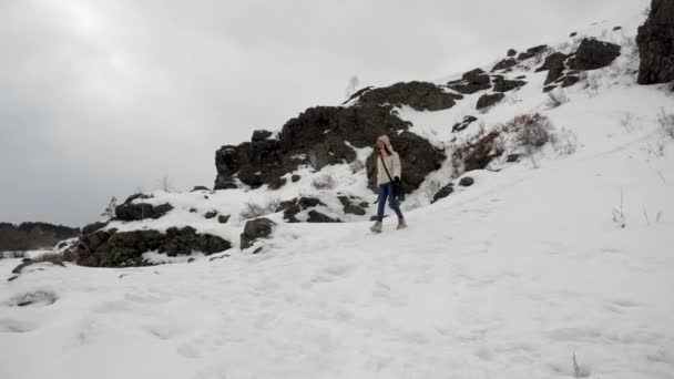 En ung flicka stiger ner från ett berg ner med utsikt över vinterskogen — Stockvideo