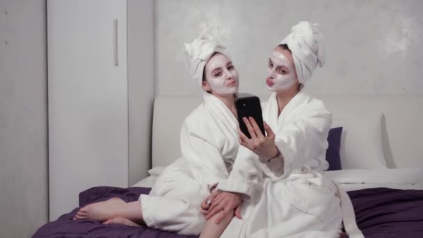 Dwie dziewczyny w szlafrokach i maskach do twarzy robią sobie selfie telefonem — Wideo stockowe