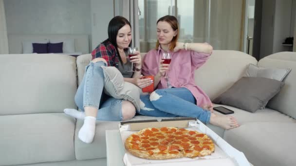 İki arkadaş neşeli bir şekilde konuşur, kırmızı şarap içer, pizza yer ve dinlenir. — Stok video