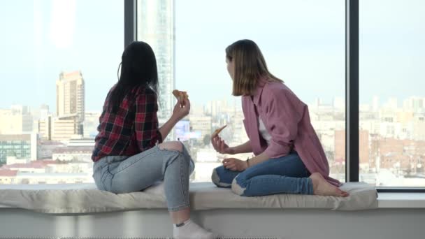 Filles assis sur un rebord de fenêtre avec une fenêtre et une vue sur la ville, manger de la pizza — Video