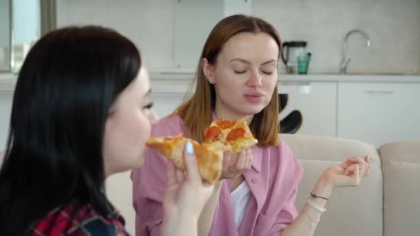 Dvě mladé přítelkyně dívky lahodně jíst pizzu a mluvit sedí doma — Stock video