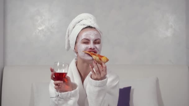 バスローブを着た女の子顔のマスクがピザを食べワインを飲む — ストック動画