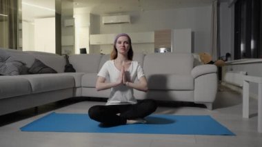 Bir kız nilüfer çiçekli bir poz verir ve dairesinde mavi yoga minderi üzerinde meditasyon yapar.