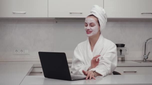 Jeune fille en peignoir, masque facial parlant joyeusement sur le portable de la caméra web — Video