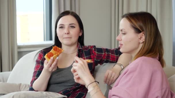 Deux filles copines mangent de la pizza et parlent assis sur un canapé dans l'appartement — Video