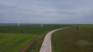 Açık havada, yeşil tarlaların ortasında beyaz rüzgar tarlaları duruyor.