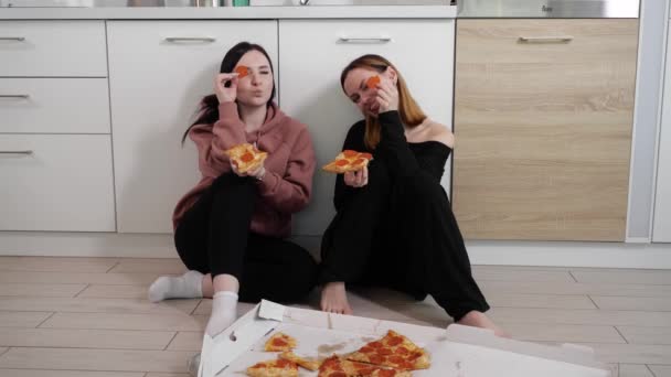 Happy young girls eat pizza and are crooked sitting at home in the kitchen — Stock Video