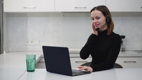 Una linda chica en un auricular auriculares hablando en la webcam de su ordenador portátil — Vídeo de stock