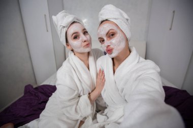 İki kız arkadaş komik suratlar yapar, selfie çekerken dudaklarını uzatırlar. 