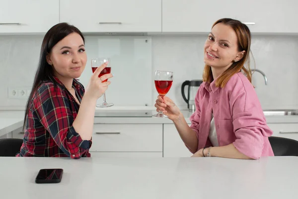 Две девушки девушки пьют красное вино сидя дома на кухне — стоковое фото