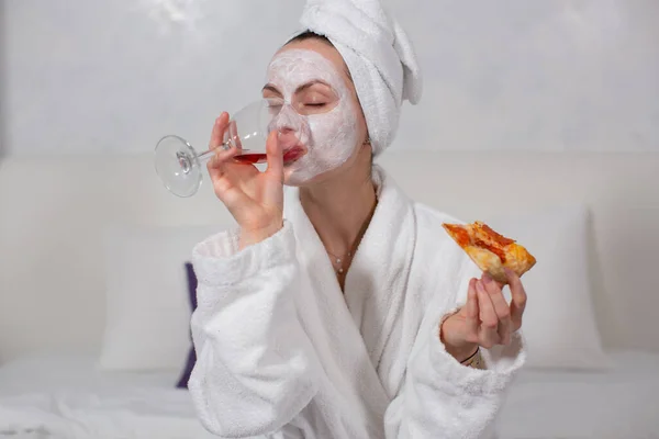 Bardaktan kırmızı şarap içen beyaz cüppeli bir kızın portresi, pizza yiyor.