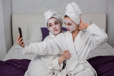 İki modern kız spa tedavisi yapıyor, telefonlarıyla selfie çekerken eğleniyorlar.