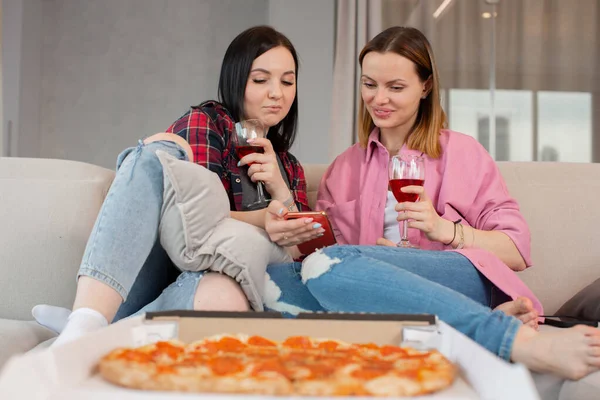 Genç kız öğrenciler eğleniyor, kırmızı şarap içiyor ve pizza yiyorlar. 