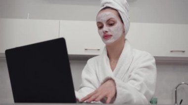 Manzara, sabahlık giymiş, dizüstü bilgisayarın arkasında çalışan yakın plan bir kız.