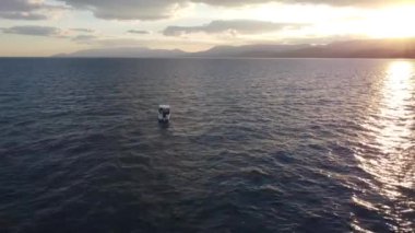 Denizde yalnız bir tekne, günbatımının arka planında ve yüksek dağlarda.