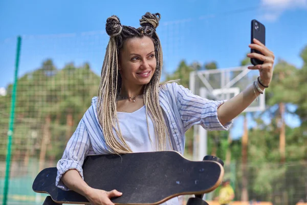 Rasta bukleli güzel bir genç kız selfie çekiyor ve elinde bir uzun tahta tutuyor.