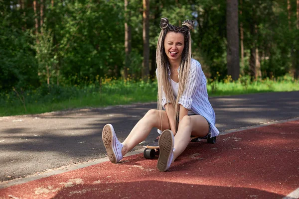 Een tienermeisje zit op een longboard en laat vrolijk haar tong zien — Stockfoto