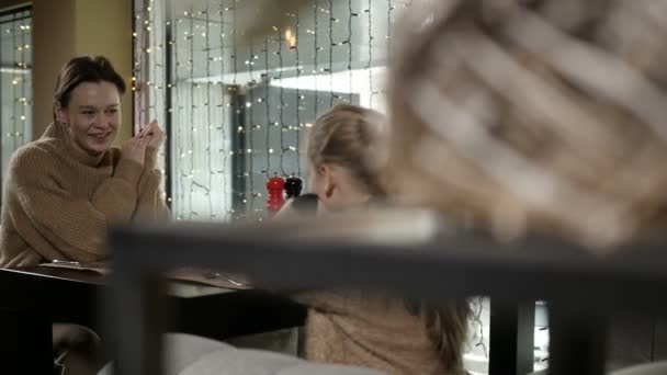 Anya és lánya ülnek egy kávézóban az azonos színű pulóverekben. — Stock videók