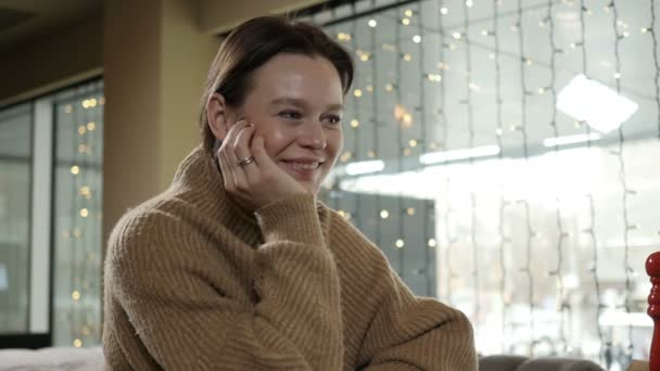 Una mujer en un suéter beige se sienta en un restaurante y habla con alguien — Vídeos de Stock
