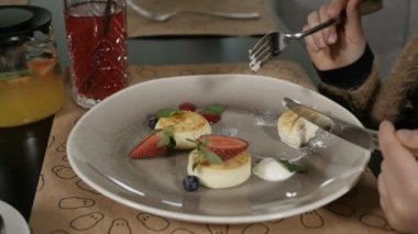 Kızların elleri beyaz tabakta duran böğürtlenli peynirli kekleri kesiyor..