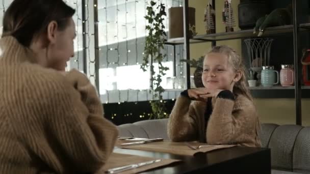Мати і маленька дочка сидять в кафе і солодко розмовляють, посміхаються — стокове відео