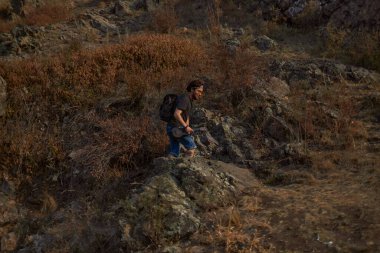 Dağlık arazide yürüyen siyah sırt çantalı bir adam.