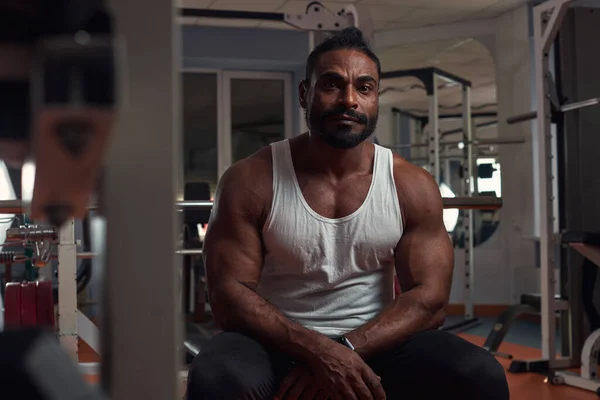 Güçlü bir atletik adam spor salonunda simülatörde oturuyor.