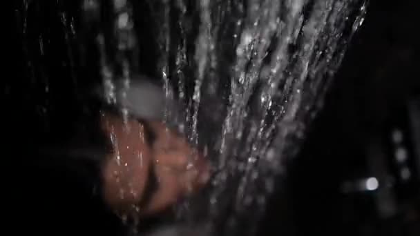 Meisje in een wit shirt staat onder de douche en streelt haar haar — Stockvideo