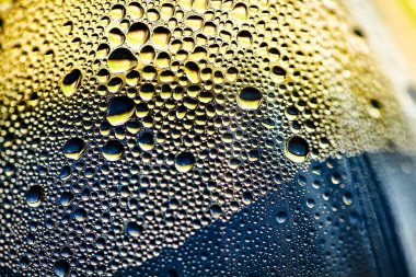 Bulanık sarı-mavi arkaplan. Plastik şişelere su damlaları. Güneşte bir damla su. Gökyüzünün dokusu, okyanus, deniz, su.