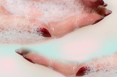 Seçici odaklanma. Soyut temizlik ve hijyen kavramı. Kız ellerini yıkıyor, covid-19. Sabun köpüğüyle el yıkamak. Sabunlu köpüklü uzun kırmızı tırnaklı bir kadın eli..