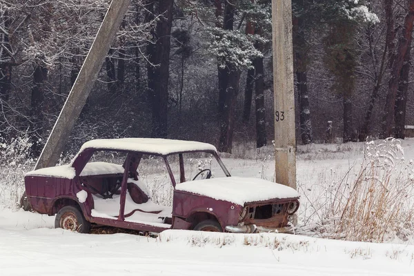 Old abandoned car in the snow near the forest.Rusty, destroyed, abandoned car in the countryside of Ukraine on a winter day.Vintage background with a car.