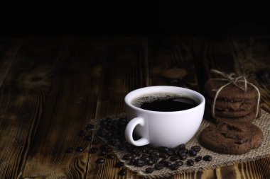 Koyu renkli ahşap masa üzerinde çikolatalı kurabiye ile beyaz fincan americano kahvesi.