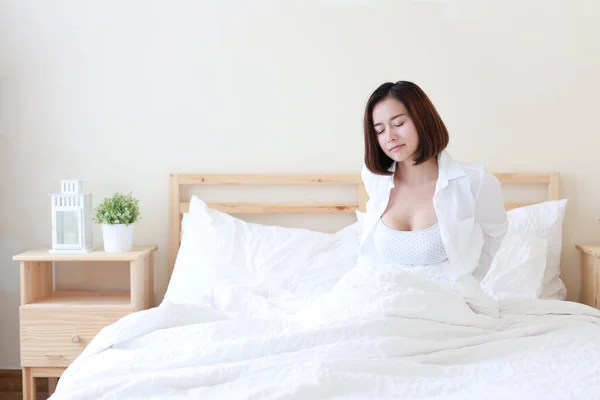 フロントビュー美しいと健康的な若いアジアの女性が目を覚ます午前中に 彼女はベッドルームで白いベッドの上で朝起きてストレッチ — ストック写真
