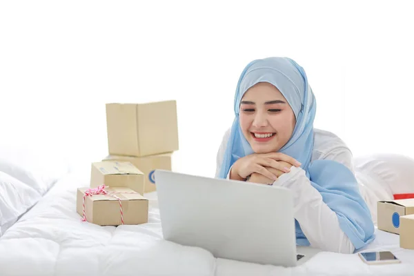 魅力的な外観を持つ寝姿で美しく 若いアジアのイスラム教徒の女性は コンピュータ 携帯電話 オンラインパッケージボックス配信とベッドの上にあります 賢いです女の子とともにHijab受信良いニュースと驚き — ストック写真