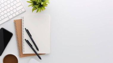 Üzerinde bilgisayar ve ofis malzemeleri olan beyaz manzaralı ahşap ofis masası. Boş defter, klavye, yeşil yaprak ve kahve fincanı olan düz bir çalışma masası. Reklam içeriğiniz için alanı kopyalayın.