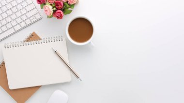Üzerinde bilgisayar ve ofis malzemeleri olan beyaz manzaralı ahşap ofis masası. Boş defter, klavye, çiçek ve kahve fincanı olan düz bir çalışma masası. Reklam içeriğiniz için alanı kopyalayın.