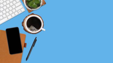 Üzerinde bilgisayar ve ofis malzemeleri olan mavi manzaralı ahşap ofis masası. Boş not defteri, klavyesi, yeşil yaprağı, kalemi, kahve fincanı olan düz bir çalışma masası. Reklam içeriğiniz için alanı kopyalayın.