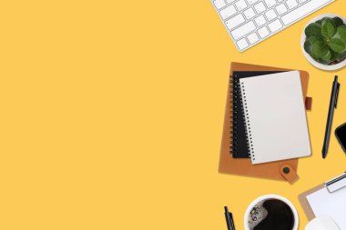 Üzerinde bilgisayar ve ofis malzemeleri olan sarı manzaralı ahşap ofis masası. Boş defter, klavye, yeşil yaprak ve kahve fincanı olan düz bir çalışma masası. Reklam içeriğiniz için alanı kopyalayın.