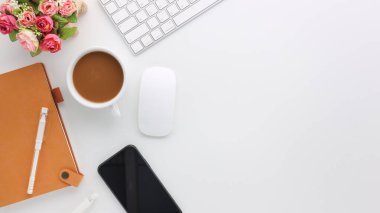 Üzerinde bilgisayar ve ofis malzemeleri olan beyaz manzaralı ahşap ofis masası. Boş defter, klavye, çiçek ve kahve fincanı olan düz bir çalışma masası. Reklam içeriğiniz için alanı kopyalayın.