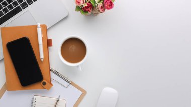 Üzerinde bilgisayar ve ofis malzemeleri olan beyaz manzaralı ahşap ofis masası. Boş defter, klavye, çiçek ve kahve fincanı olan düz bir çalışma masası. Reklam içeriğiniz için alanı kopyalayın.
