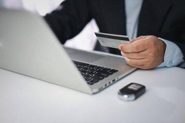 Siyah takım elbiseli bir adam oturuyor, kredi kartı tutuyor ve akıllı telefonu sadece aylık araba ödemesi ya da internetten alışveriş yapmak için kullanıyor. Dizüstü bilgisayar kullanan bir iş adamı.