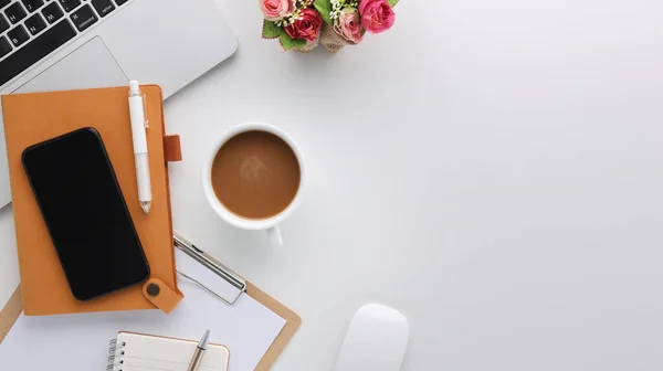 Top view white wooden workspace office desk with computer and office supplies. Flat lay work table with blank notebook, keyboard, flower and coffee cup. Copy space for your advertising content.