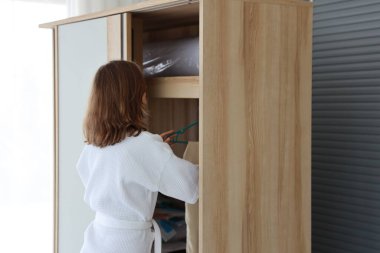 Arkadan bakınca beyaz pijamalı beyaz bir kadın yatak odasında kıyafet seçiyor (yaşam tarzı ve rahatlama konsepti))