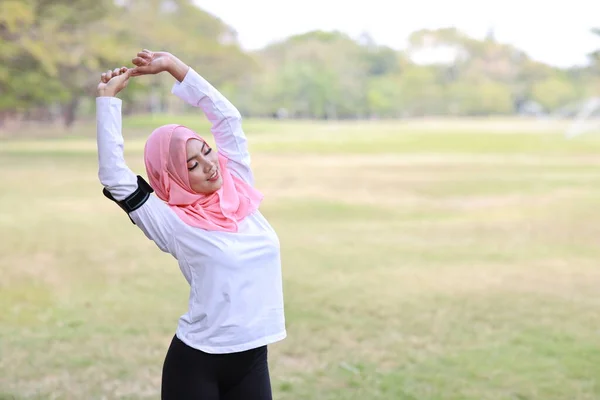 公共锻炼生活方式理念 健身女性通过无线耳机和手机听音乐 侧视运动年轻的亚洲穆斯林女子穿着运动服站着 运动后伸展着 — 图库照片