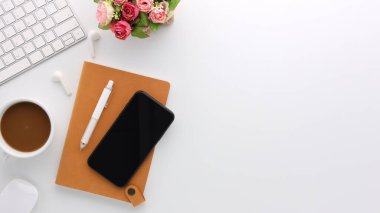 Üzerinde bilgisayar ve ofis malzemeleri olan beyaz manzaralı ahşap ofis masası. Boş defter, klavye, çiçek ve kahve fincanı olan düz bir çalışma masası. Reklam içeriğiniz için alanı kopyalayın.