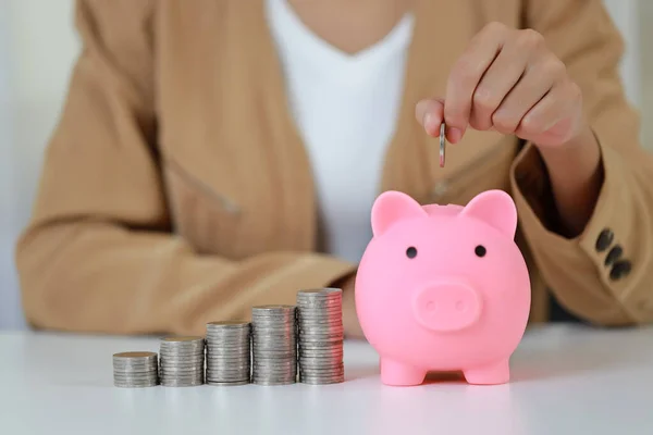 Smart and active asian businesswoman hands putting coin into piggy bank with saving growth on stacking coin on table, meaning of earning money or investment or tax for business advertising concept